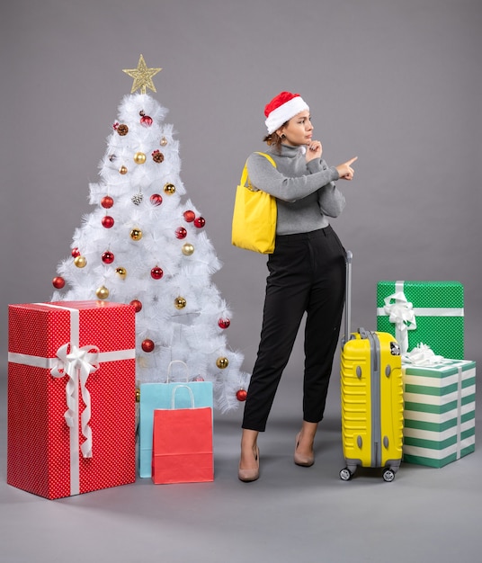 Foto gratuita mujer vistiendo gorro de papá noel con equipaje junto al árbol de navidad