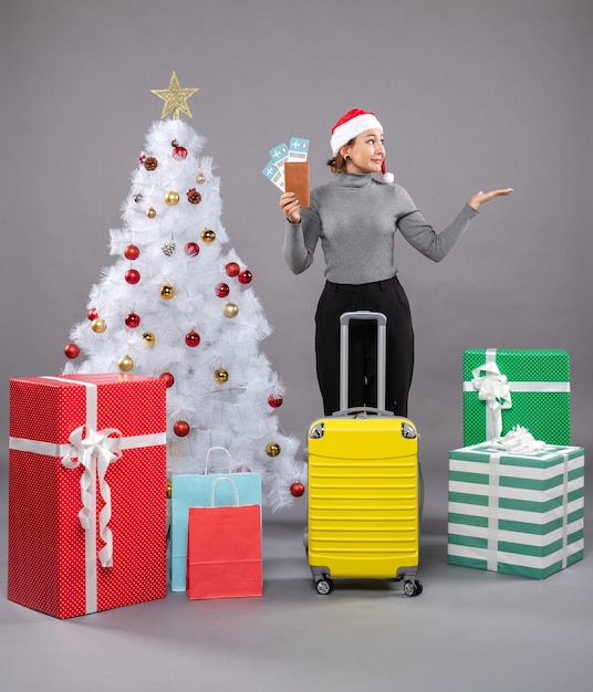 Foto gratuita mujer vistiendo gorro de papá noel con equipaje junto al árbol de navidad