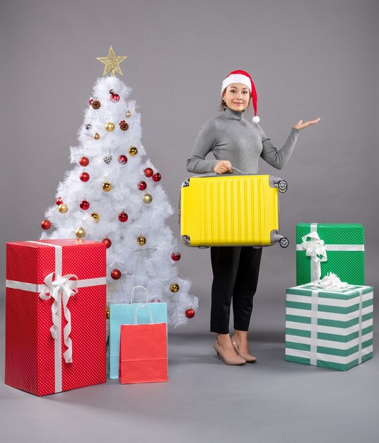 Mujer vistiendo gorro de Papá Noel sujetando el equipaje junto al árbol de Navidad