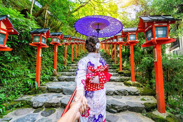 Mujer vistiendo kimono tradicional japonés sosteniendo la mano del hombre y llevándolo al santuario Kifune, Kyoto en Japón.