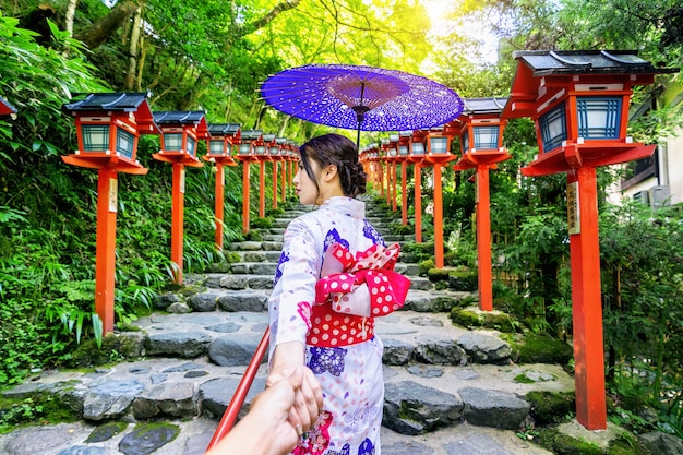 Mujer vistiendo kimono tradicional japonés sosteniendo la mano del hombre y llevándolo al santuario Kifune, Kyoto en Japón.