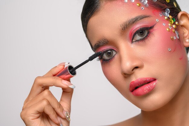 Mujer vistiendo maquillaje rosa y cepillado de cejas aislado en blanco