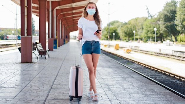 Foto gratuita mujer vistiendo máscara de tiro completo con equipaje en la estación de tren