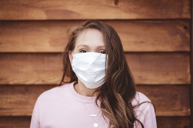 Foto gratuita mujer vistiendo una mascarilla sanitaria delante de una pared de madera