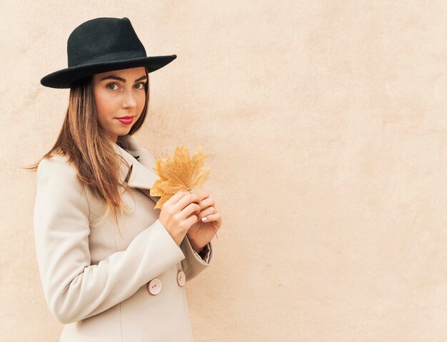 Mujer vistiendo un sombrero negro y sosteniendo una hoja