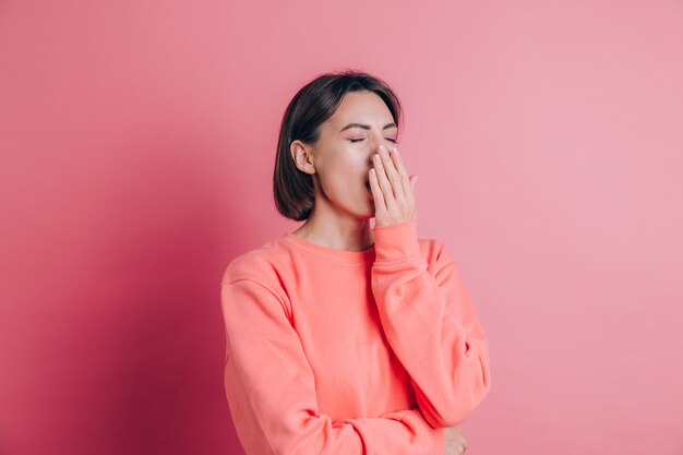 Mujer vistiendo un suéter casual en el fondo aburrido bostezo cansado cubriendo la boca con la mano. Inquietud y somnolencia