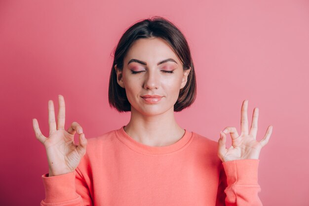 Mujer vistiendo un suéter casual en el fondo relajarse y sonreír con los ojos cerrados haciendo gesto de meditación con los dedos. Concepto de yoga.