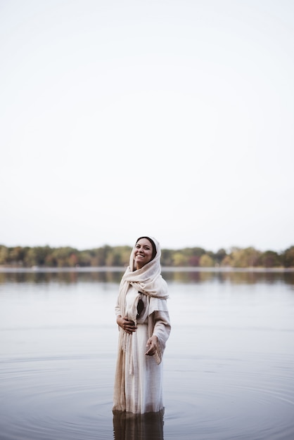 Mujer vistiendo una túnica bíblica mientras está de pie en el agua y sonriendo