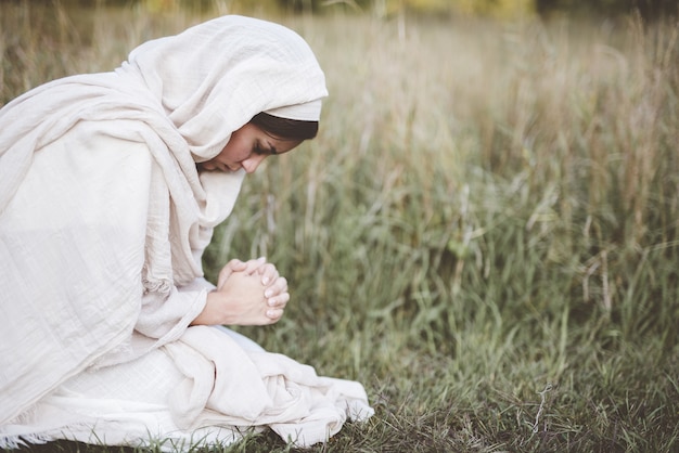 Mujer vistiendo una túnica bíblica y de rodillas mientras reza