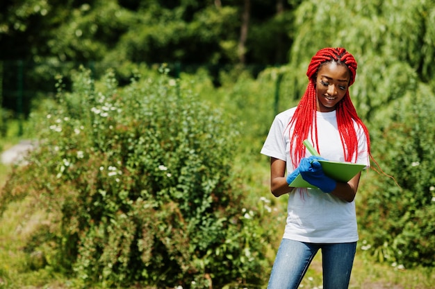 Mujer voluntaria pelirroja africana con portapapeles en el parque África voluntariado personas caritativas y concepto de ecología