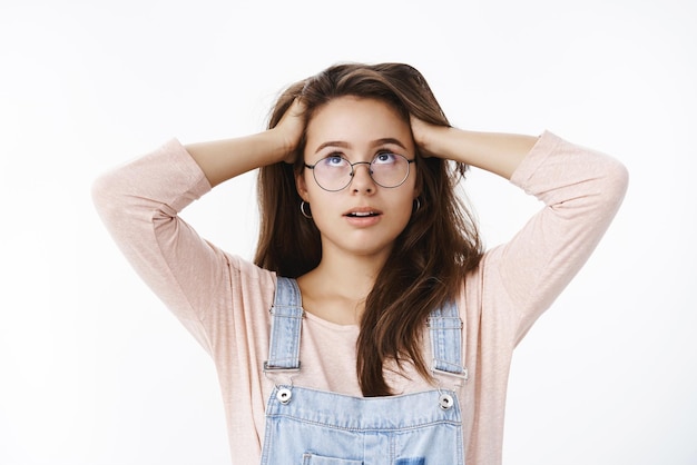 La mujer se vuelve loca porque se siente molesta y harta de enviar mensajes con las manos debajo del cabello, los ojos en blanco, irritada y enojada, de pie, tensa y presionada sobre un fondo gris