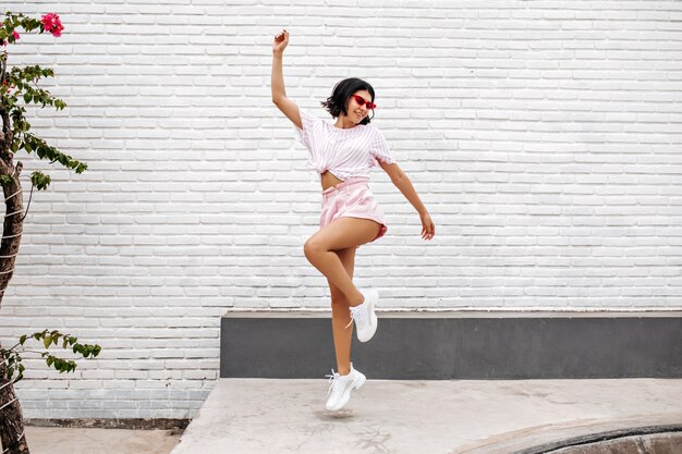 mujer en zapatillas blancas saltando en la calle. Vista de longitud completa de la mujer bailando disfrutando del verano.