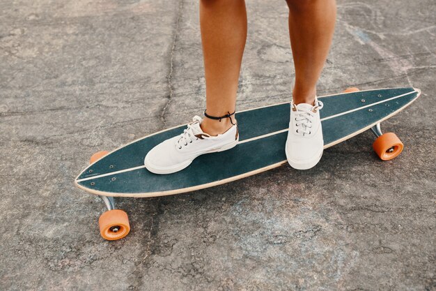 Mujer en zapatillas montando patineta al aire libre en la superficie de asfalto.