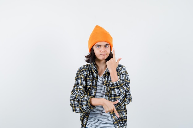 Mujercita apuntando hacia arriba y hacia abajo en gorro de chaqueta de camiseta mirando confiado