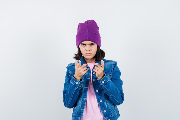 Mujercita apuntando a la cámara en chaqueta de mezclilla y gorro mirando serio