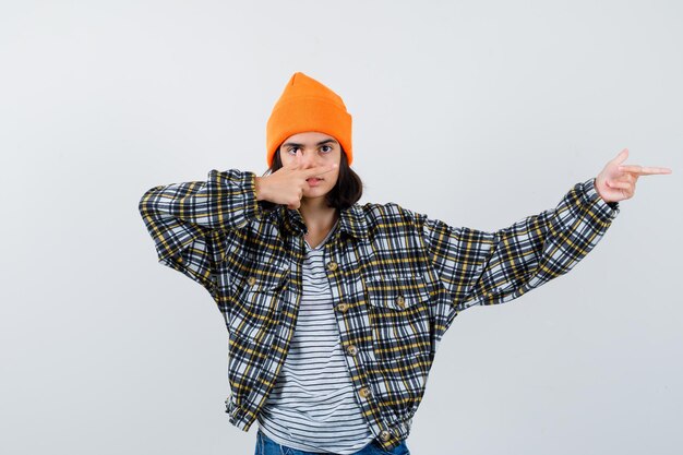 Mujercita apuntando hacia el lado derecho en camiseta y chaqueta mirando confiado