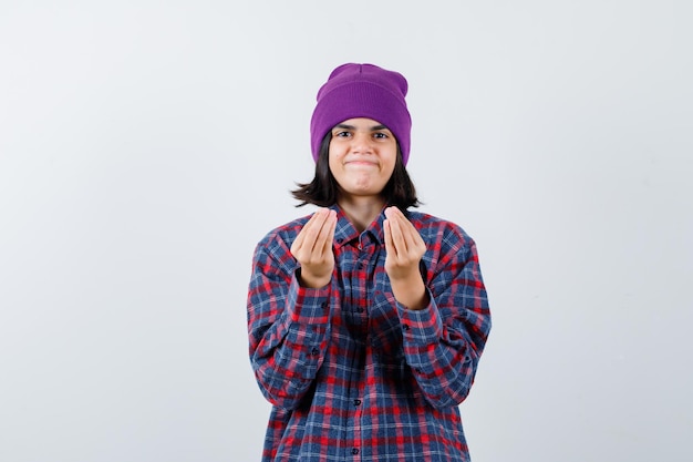 Mujercita en camisa a cuadros y gorro mostrando gesto italiano y mirando encantada