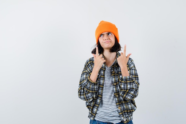 Foto gratuita mujercita en gorro de chaqueta de camiseta apuntando hacia arriba mirando vacilante