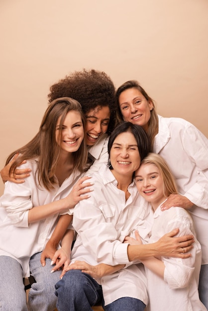 Foto gratuita mujeres africanas caucásicas alegres de diferentes edades en camisas blancas riéndose mirando la cámara sobre fondo beige