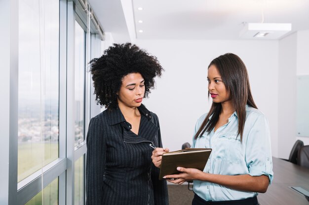 Mujeres afroamericanas con documentos cerca de la ventana en la oficina