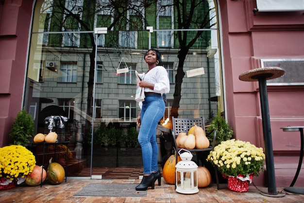 Mujeres afroamericanas con estilo en blusa blanca y jeans azules posaron cerca de un café con periódico