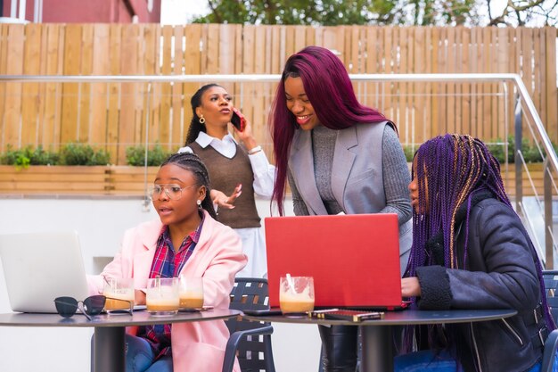 Mujeres afroamericanas en una reunión de negocios en una cafetería con computadoras portátiles y café en la mesa