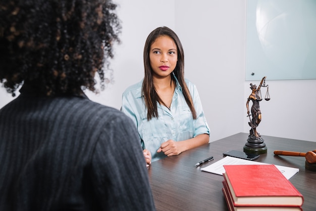 Foto gratuita mujeres afroamericanas sentadas a la mesa cerca de documento, pluma, figura y martillo