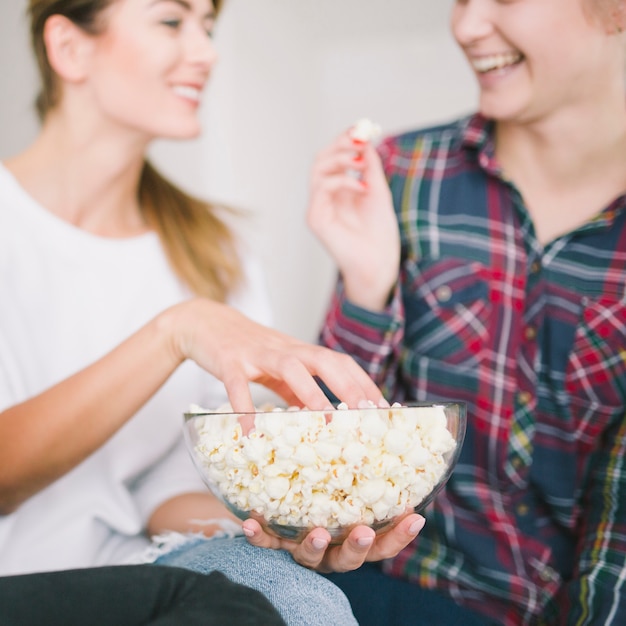 Mujeres alegres compartiendo palomitas de refrigeración en el sofá