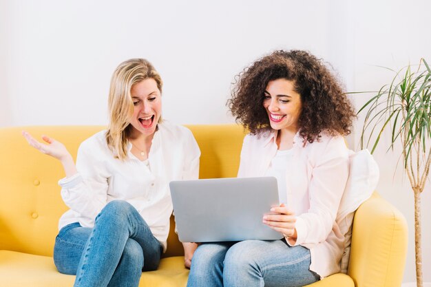 Mujeres alegres con la computadora portátil en el sofá