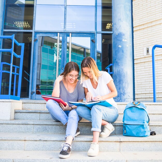 Mujeres alegres que estudian en pasos de la universidad