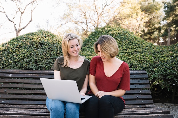 Mujeres alegres que navegan la computadora portátil en parque