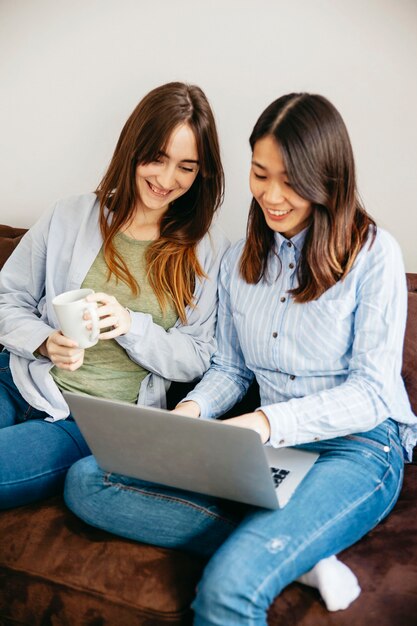 Mujeres alegres que navegan la computadora portátil en el sofá