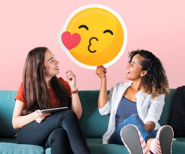 Mujeres alegres sosteniendo un icono de emoticon besándose
