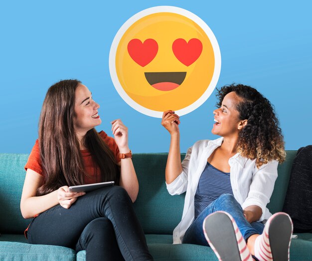 Mujeres alegres sosteniendo un icono de emoticon de ojos de corazón