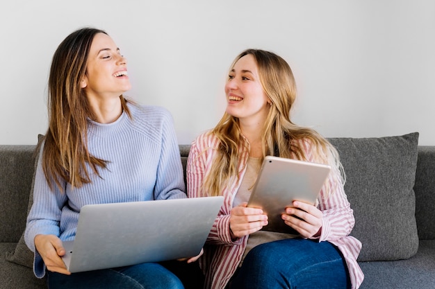 Mujeres alegres con tableta y computadora portátil