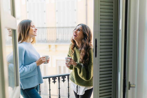 Mujeres alegres con tazas en el balcón