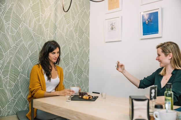 Mujeres alegres tomando fotos en café