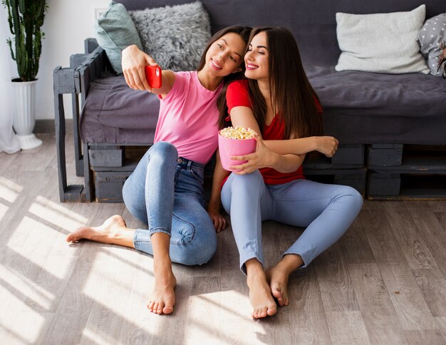 Mujeres de alto ángulo comiendo palomitas de maíz y tomando selfie