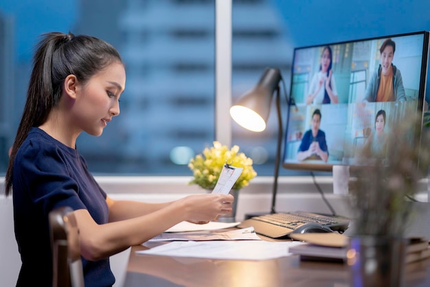 Foto gratuita las mujeres asiáticas adultas jóvenes inteligentes usan ropa informal trabajando tarde en la noche en una reunión de teleconferencia en casa en línea con socios comerciales concepto de cuarentena de aislamiento en el hogar