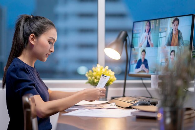 Las mujeres asiáticas adultas jóvenes inteligentes usan ropa informal trabajando tarde en la noche en una reunión de teleconferencia en casa en línea con socios comerciales concepto de cuarentena de aislamiento en el hogar