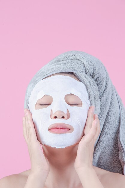 Las mujeres asiáticas hermosas están utilizando la cara de la mascarilla en la hoja en un fondo rosado.