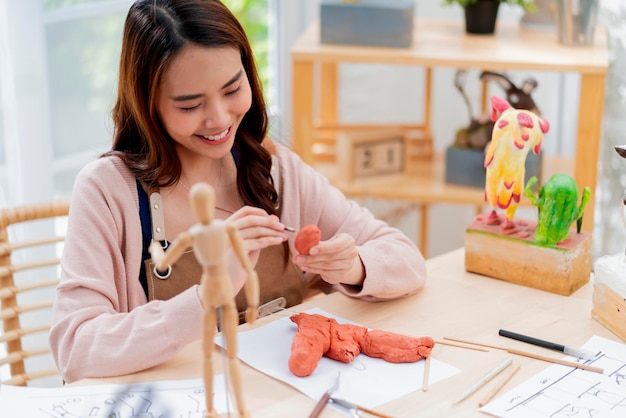 Las mujeres asiáticas pasan el fin de semana para su curso en línea de escultura de arcilla de hobby en casa, adultos jóvenes que estudian desde un curso de transmisión de tabletas en línea en un estilo de vida informal asiático disfrazado de delantal en casa