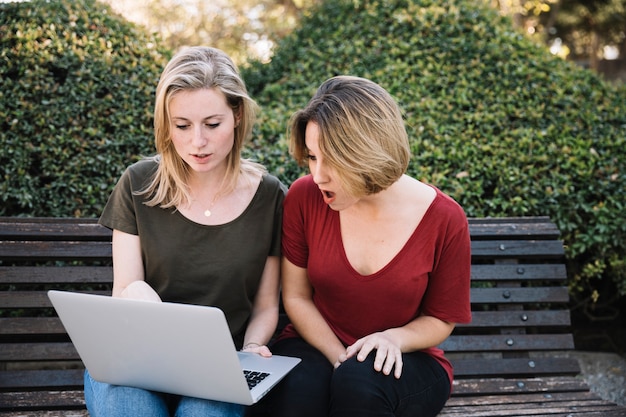 Mujeres asombradas que usan la computadora portátil en parque