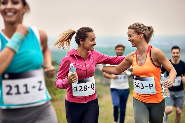 Mujeres atléticas felices apoyándose mutuamente mientras corren un maratón en la naturaleza