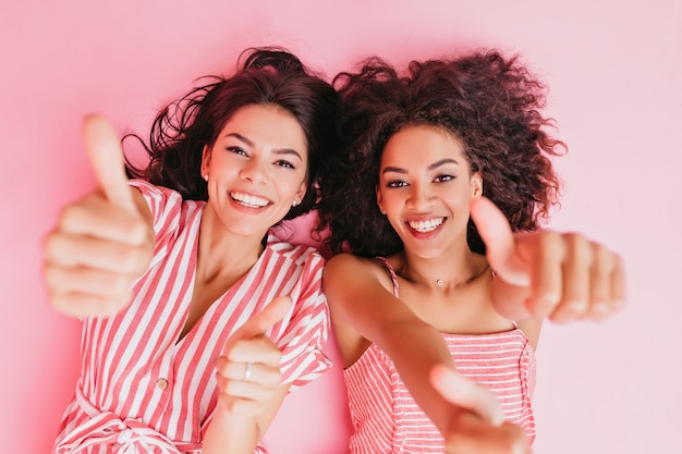 Foto gratuita las mujeres atractivas se iluminan de alegría y muestran grandes pulgares hacia arriba. alegres chicas de pelo oscuro