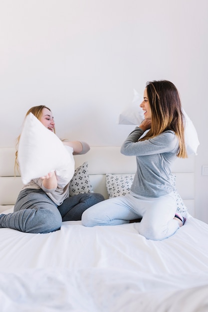 Mujeres atractivas que tienen almohada luchan en la cama