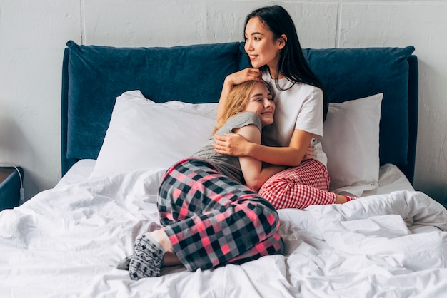 Mujeres atractivas sentadas en la cama abrazando fuertemente