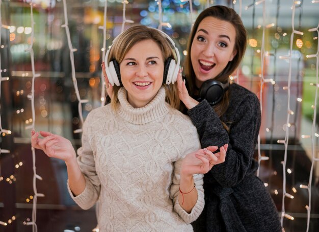 Mujeres con auriculares divirtiéndose alrededor de las luces de navidad