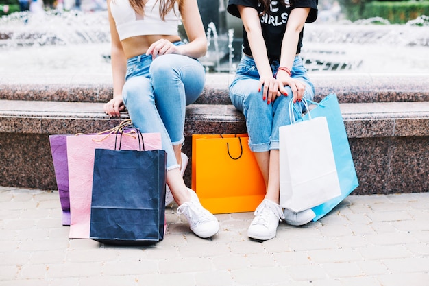 Mujeres con bolsas de papel sentado en la fuente