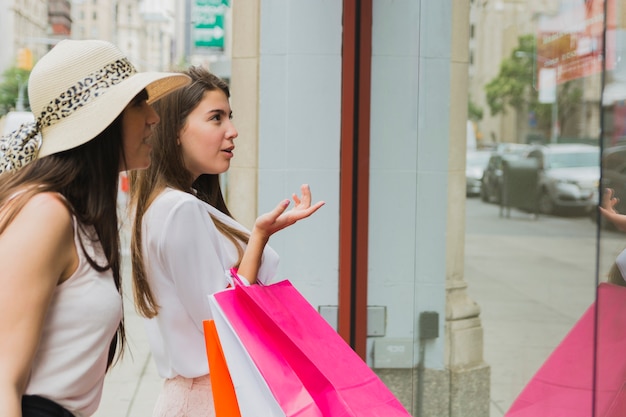 Mujeres bonitas con bolsas de compras cerca de la ventana de la tienda